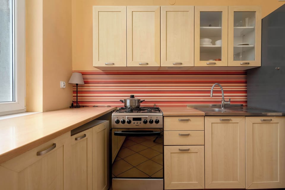 A kitchen with light wooden cabinets and a tiled backsplash in warm tones. Built-in appliances are neatly arranged. The space looks practical and well organized.