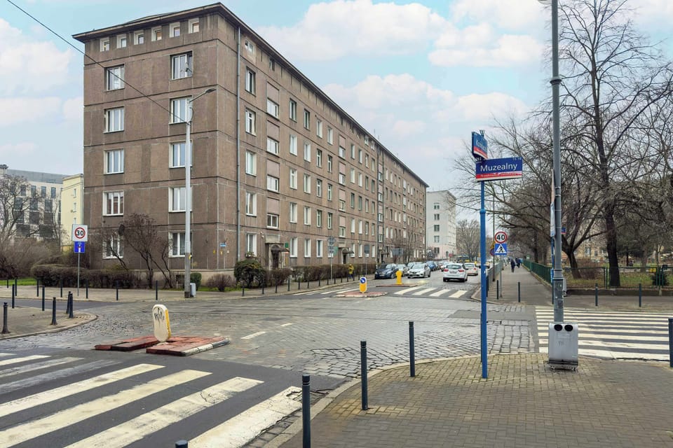 A wider street view showing apartment blocks along a sidewalk. Cars and pedestrian paths are visible. The environment feels urban and everyday.