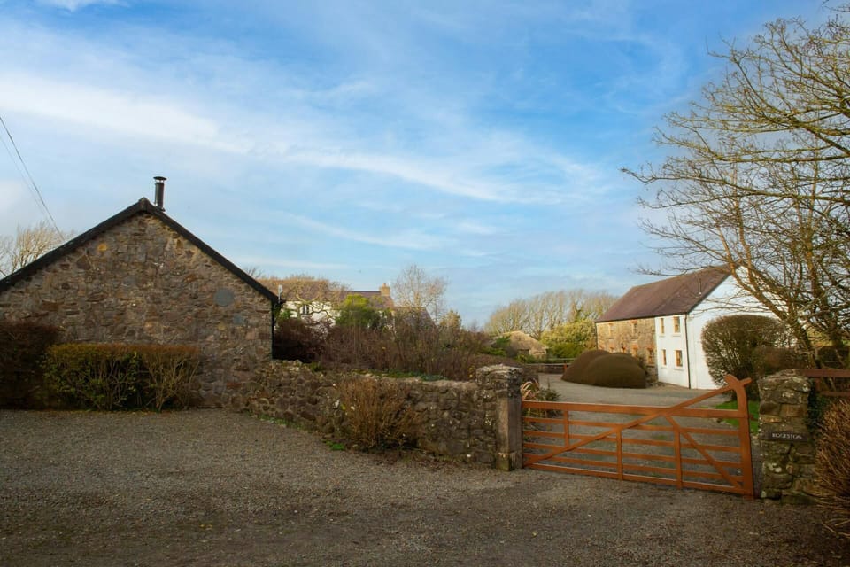 Gravel yard with stone walls, wooden gate and two houses under a blue sky