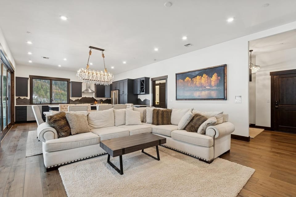 Sink into plush sectional seating where crystal chandeliers cast warm light over your open-concept living space, perfectly connected to a sleek modern kitchen.