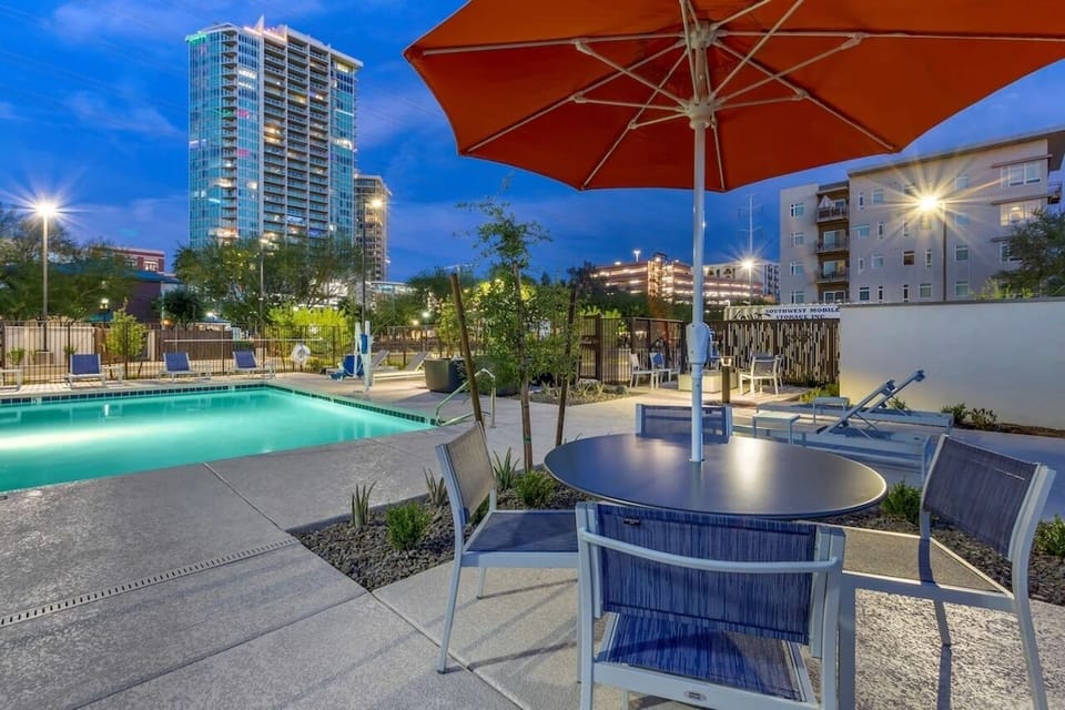 Lounge poolside at dusk with cocktails under bright umbrellas.