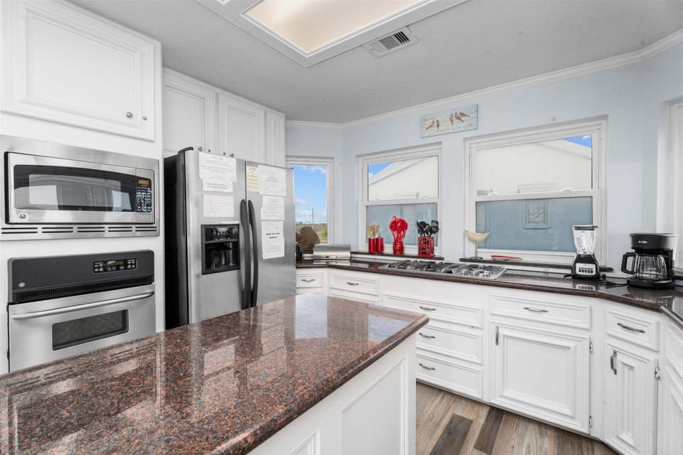Bright beachfront kitchen with granite countertops, stainless steel refrigerator, and large windows bringing in natural light and beautiful coastal views.