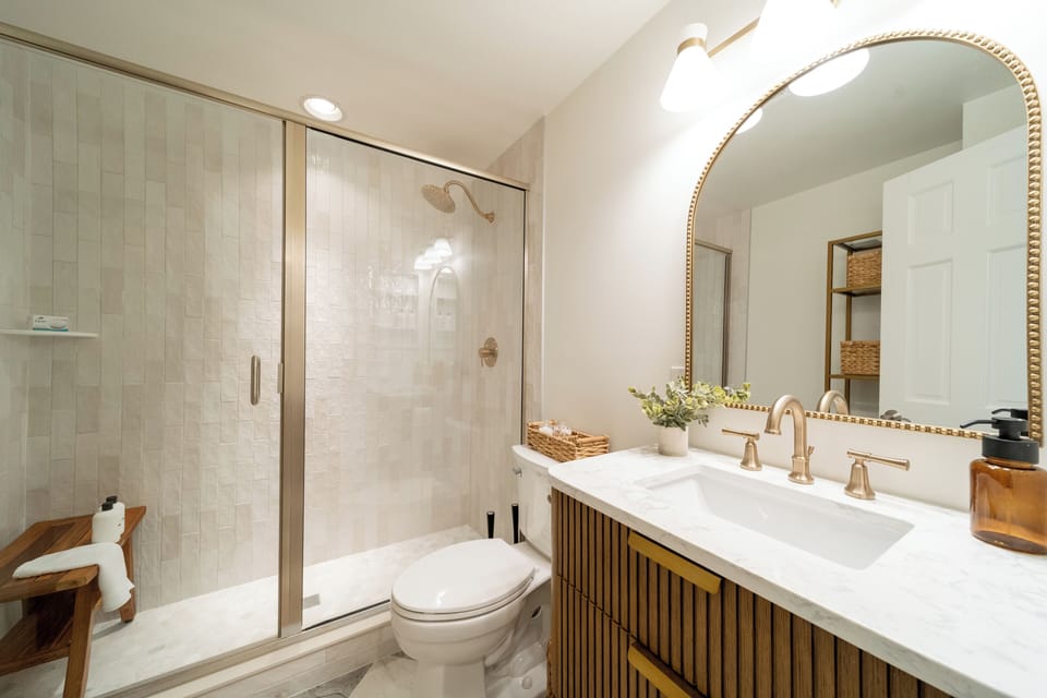 Luxury remodeled bathroom with walk-in glass rain shower and elegant modern finishes. Custom vanity with marble countertop and ample storage