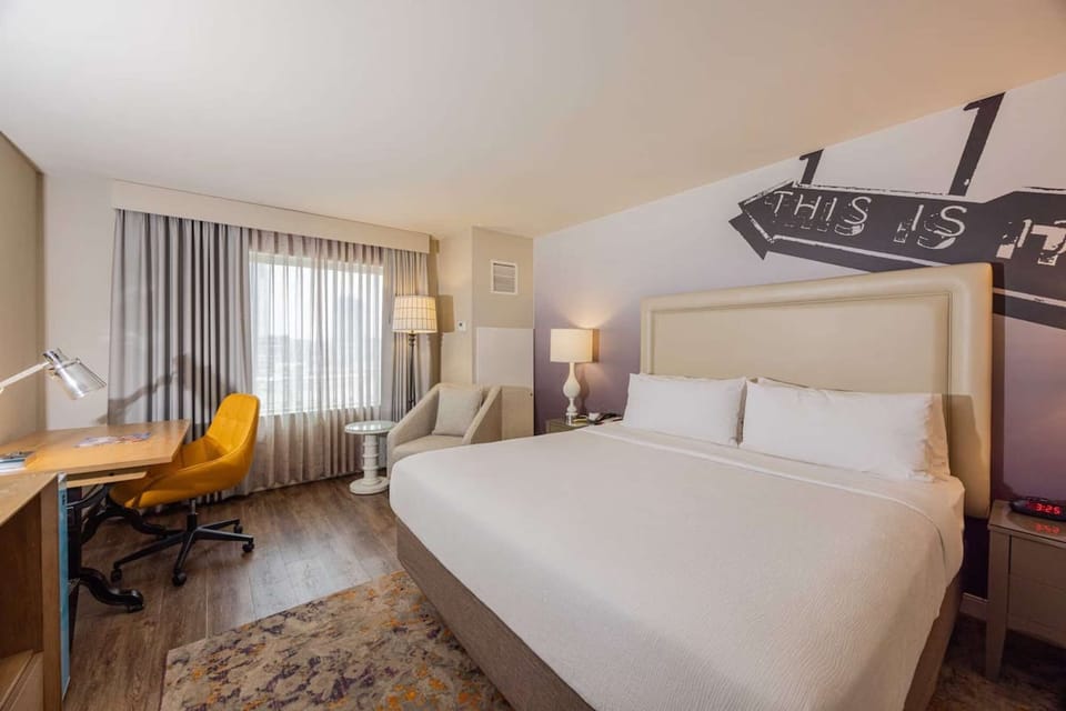 King bed, desk with chair, window with curtain, and soft lighting
