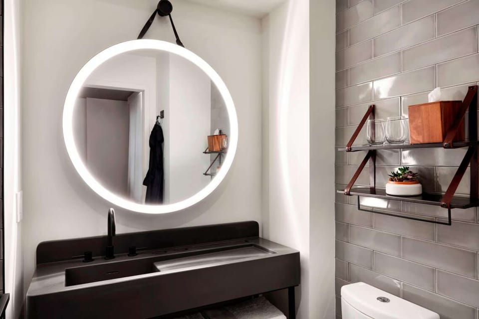 Minimal vanity with circular mirror, dark sink, and shelf accents