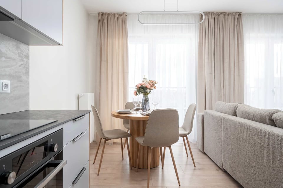 A dining and living area combined, featuring a table near the sofa and large windows letting in natural light.