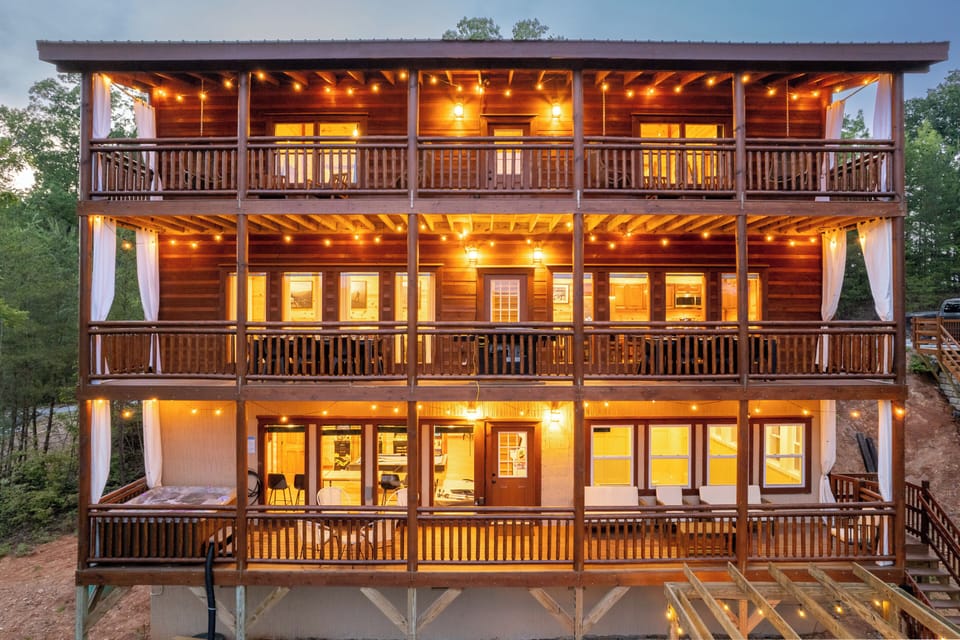 Stunning multi-level cabin with wraparound balconies, warm wood architecture, and glowing evening lights. Perfect for large groups, this spacious cabin offers beautiful views, multiple outdoor seating areas, and a welcoming mountain-lodge atmosphere.