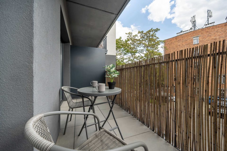 The balcony with a bistro set and bamboo screen creates a cozy spot for relaxing outdoors.
