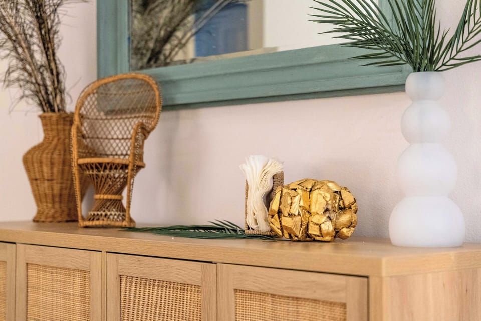 Boho-chic console with rattan, palm greens, and a gilded accent.