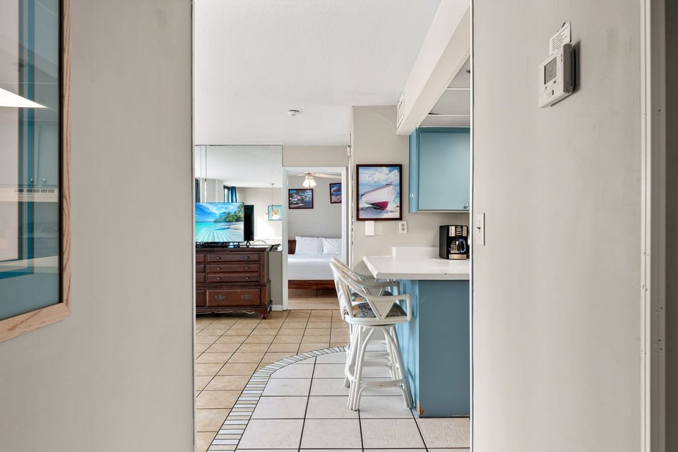 View from the kitchen area into the cozy bedroom with a classic wooden dresser and wall art.
