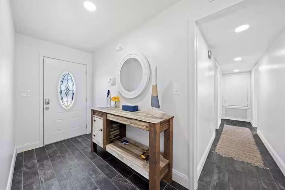 Entryway with rustic wooden console and decorative oval mirror in a bright, modern space.