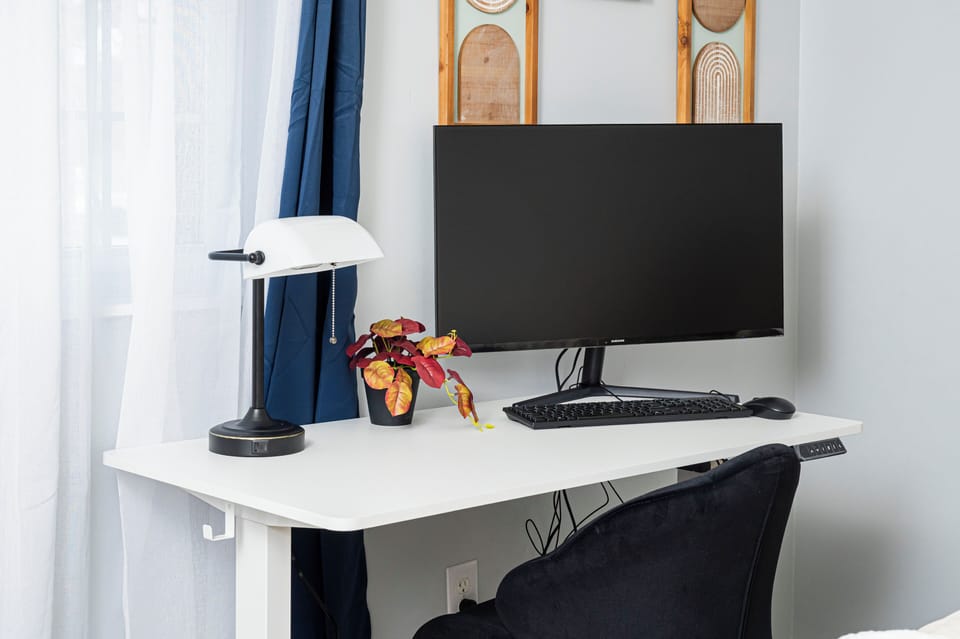 Clean workstation with standing desk, monitor, chair, lamp, and natural light