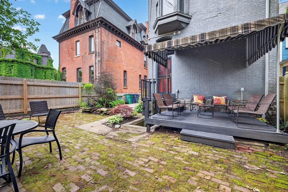 **Historic Courtyard Escape** A charming urban backyard featuring a raised wooden deck with comfortable lounge chairs and a classic striped awning. Surrounded by a rustic brick patio and historic brick buildings, it’s a serene retreat.