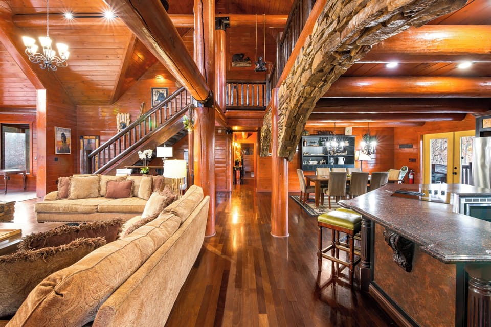 Open-concept great room with soaring ceilings, stone fireplace & panoramic forest views.