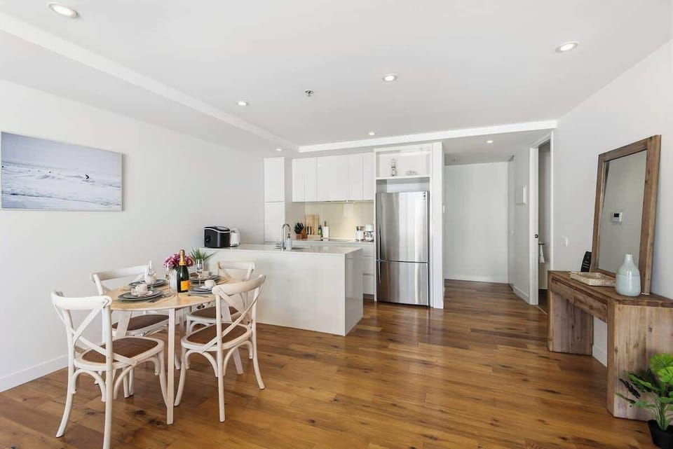 Kitchen and dining area with modern white cabinetry, wooden table set for four and bright lighting creating a welcoming space for meals.