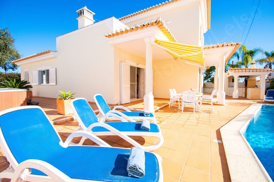 Poolside sun terrace at Casa Destino villa with comfortable blue and white sun loungers, rolled towels and a sparkling private swimming pool, featuring a shaded outdoor kitchen and barbecue area perfect for relaxing pool days during your Algarve holiday near Lagos, Portugal