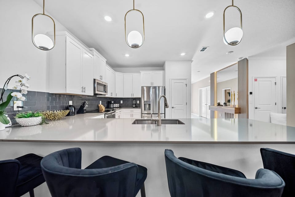 Welcome to this stunning kitchen, where sleek white cabinetry and a bold dark backsplash create a captivating look. Enjoy the warm glow of elegant pendant lights over the spacious island, ideal for casual dining or entertaining.