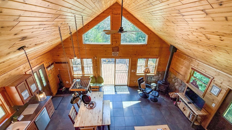 Soaring ceilings and warm wood tones create an inviting great room where you can gather around the cozy wood-burning stove or enjoy natural light streaming through expansive windows overlooking the deck.