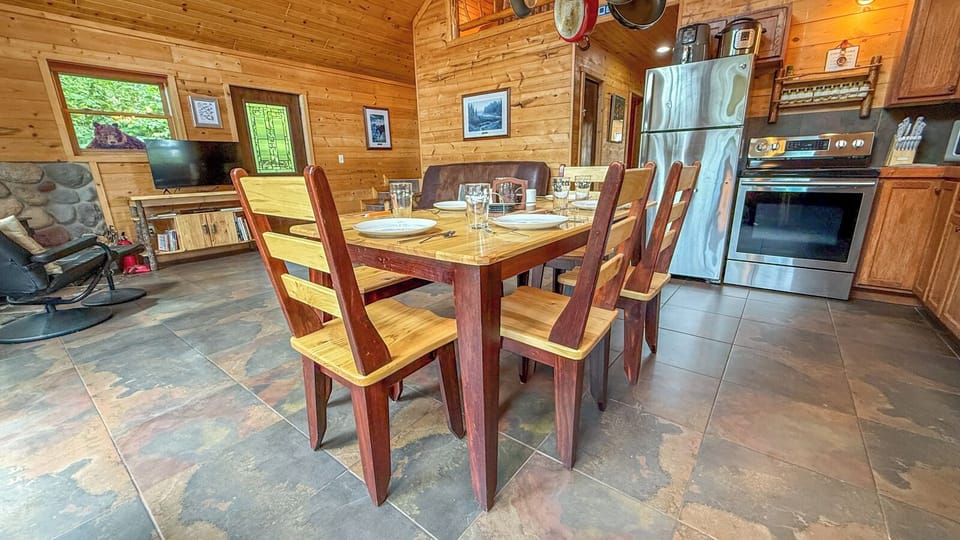 Picture yourself gathering around this handcrafted dining table for family meals in your cozy cabin. Warm wood walls, full kitchen with stainless appliances, and a stone fireplace create the perfect mountain getaway atmosphere.