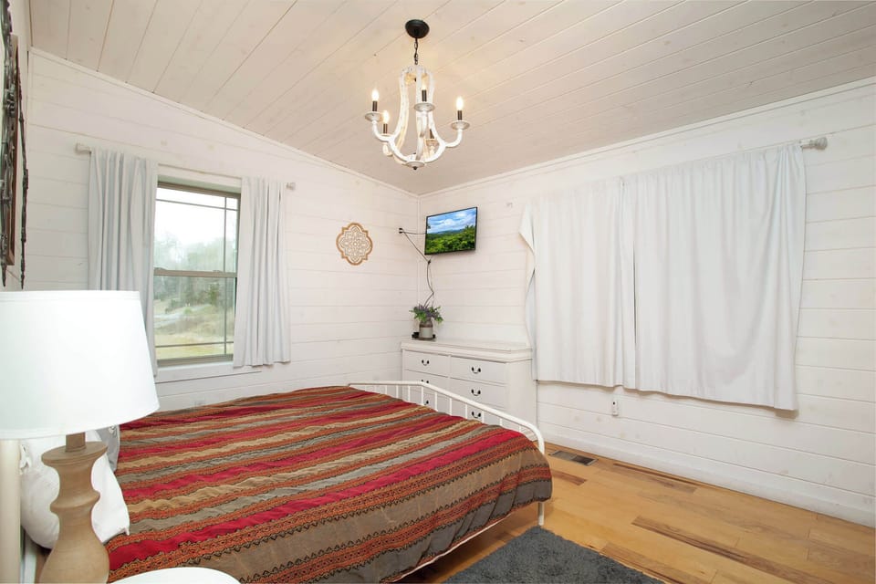 Retreat to the second bedroom, featuring a rustic chandelier, wall-mounted TV, and cozy decor.