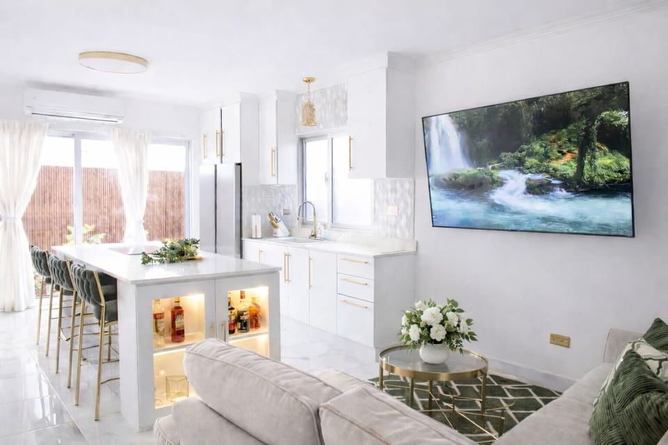 Bright modern kitchen and lounge with island seating, TV, and natural light.