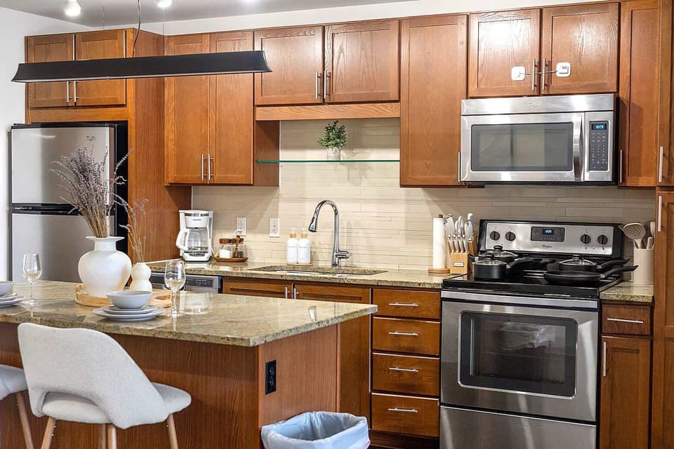Fully equipped kitchen with warm wood cabinetry, granite countertops, and stainless steel appliances. Designed for easy meal prep with ample counter space, modern finishes, and everything needed for short or extended stays.