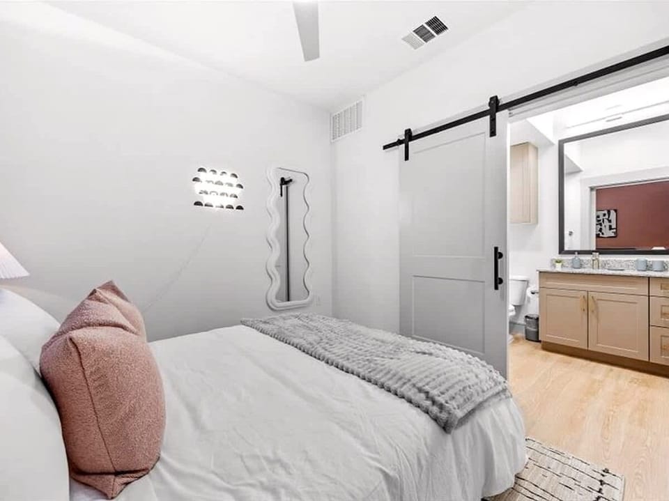 This inviting bedroom features a plush, neatly made bed with soft linens and cozy accent pillows, creating a calm retreat after a long day. Sliding barn doors lead to a modern ensuite bathroom, adding both style and convenience for a comfortable stay
