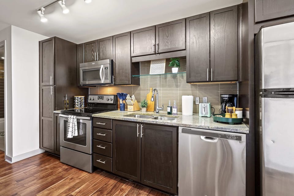Step into this sleek, modern kitchen featuring rich dark cabinetry, stainless steel appliances, and warm wood floors. Fully equipped and thoughtfully laid out, it’s perfect for cooking, entertaining, and enjoying meals with ease and style. ✨🍽️