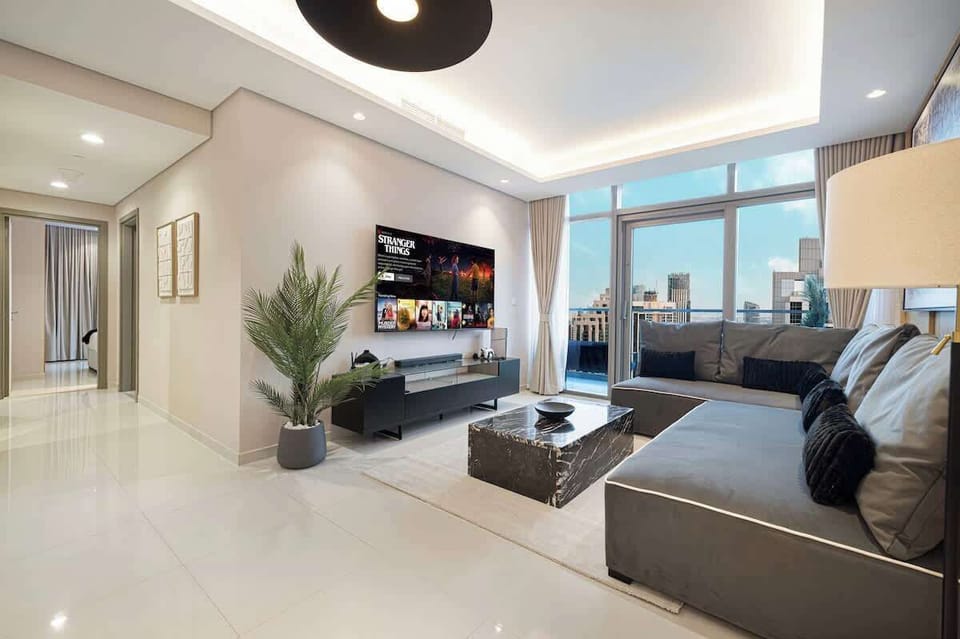 Spacious open-layout living area bathed in natural light, offering skyline views of Business Bay, a comfortable seating area, large TV, and PS5 for movie nights or gaming