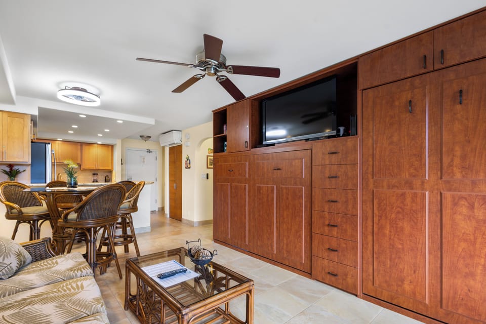 Relax in your spacious living area with rich wood cabinetry, modern entertainment center, and tropical-style dining space.