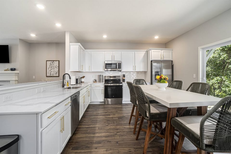 Kitchen with stainless  steel appliances, white shaker cabinets, and a large island perfect for cooking or gathering. The spacious dining area seats six comfortably, with plenty of natural light and views of the surrounding greenery.