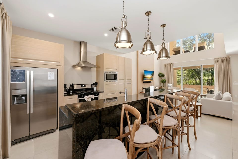 Modern kitchen with a large granite island and stainless steel appliances overlooking the living area.