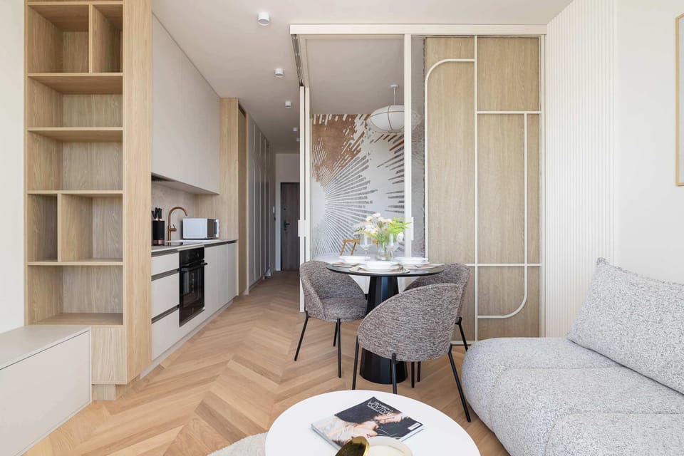 A compact living area with a corner sofa and a coffee table, connected to the kitchen, with light wood finishes.