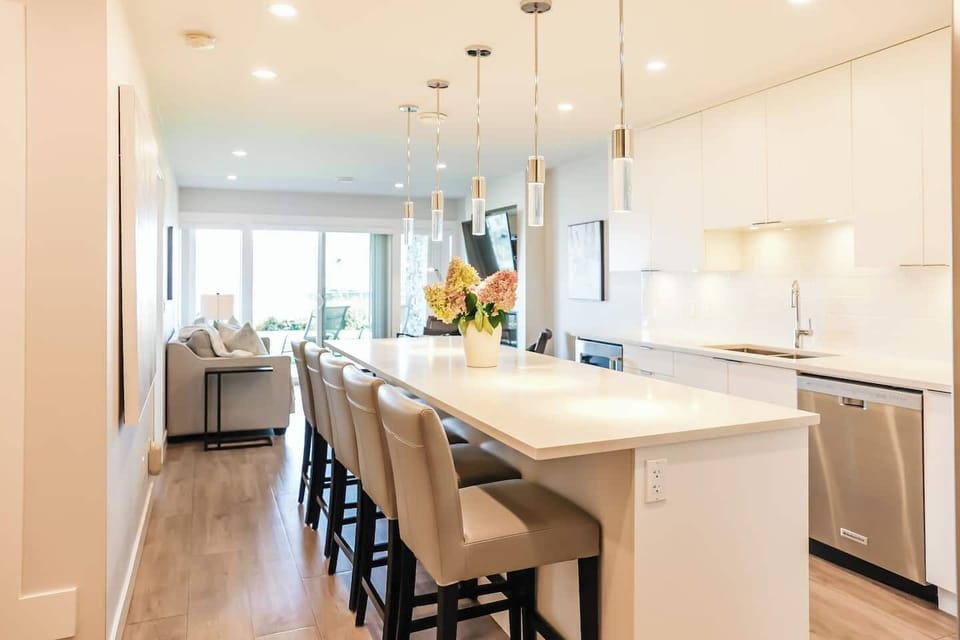 Modern kitchen with white cabinets, stainless steel appliances, and seating for six. Bright, open dining and living areas.