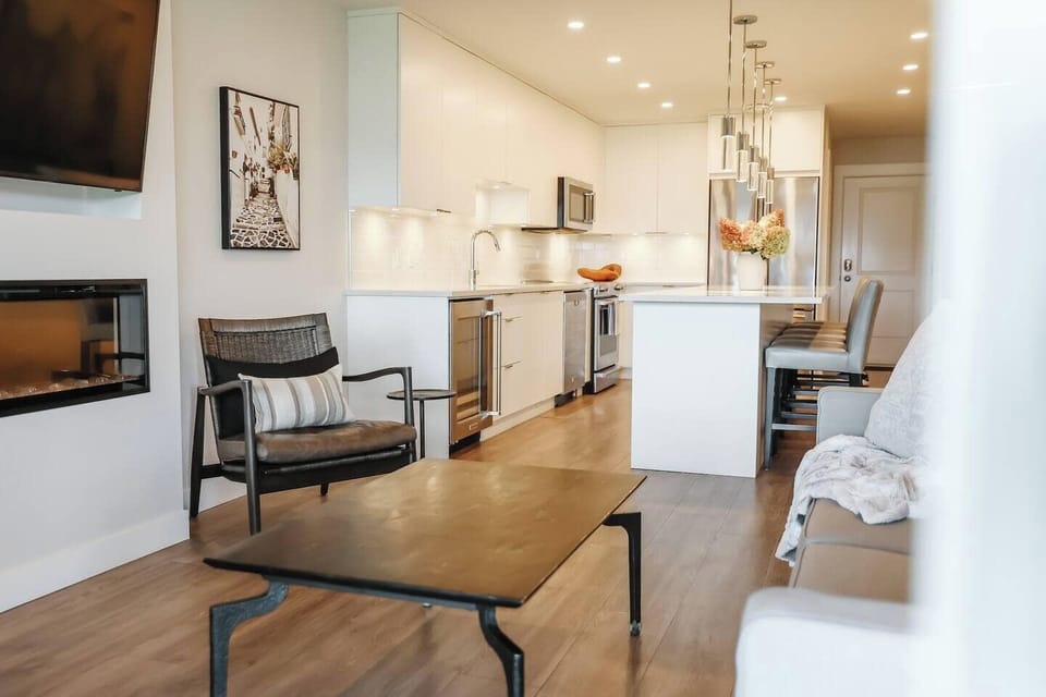 Open-concept space with a modern armchair, coffee table, and kitchen with white cabinets, stainless appliances, and a peninsula.