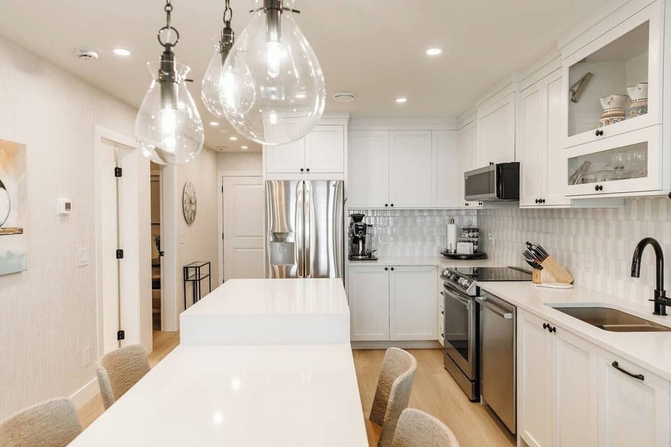 Sleek modern kitchen featuring white cabinetry, a white countertop, black bar stools, and tiled flooring.