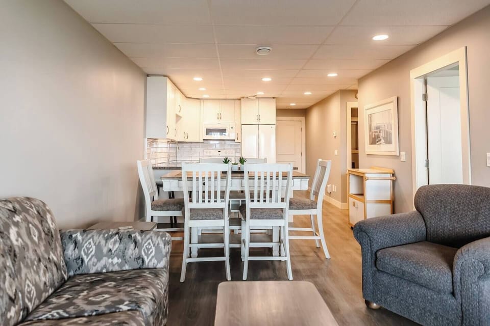 Open-concept living area featuring a mix of single and full-size couches, a coffee table, and a modern kitchen with white cabinets, appliances, and a functional peninsula.