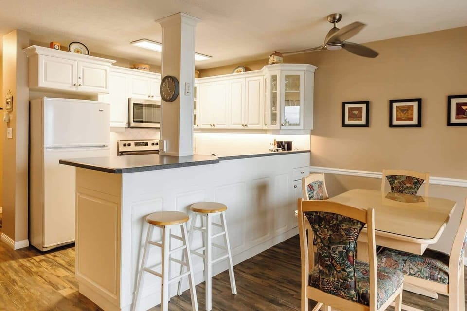 Kitchen with a breakfast bar, two bar stools, and appliances including a stove, microwave, and refrigerator.

