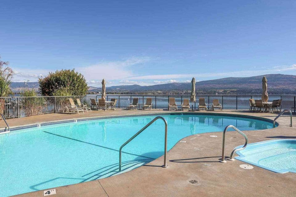 Swimming pool with blue water and a concrete deck, framed by a metal railing and stunning lake and mountain views