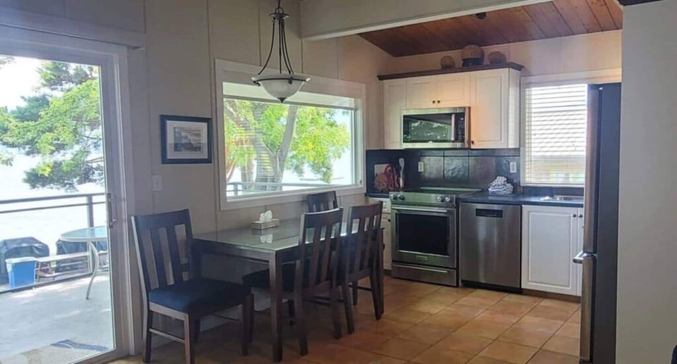 Kitchen with dark wood cabinets, black appliances, and a dining area with a wooden table and scenic window views.
