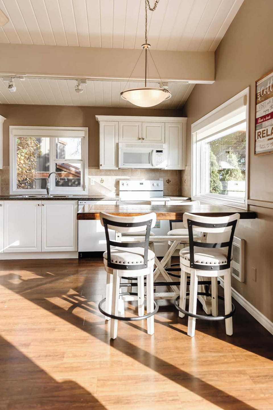 Bright kitchen with white appliances, wooden floors, and a table with bar stools for casual dining.