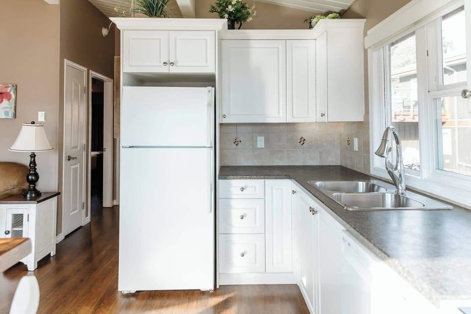 Modern kitchen with white appliances, wooden floors, and elegant black countertops.