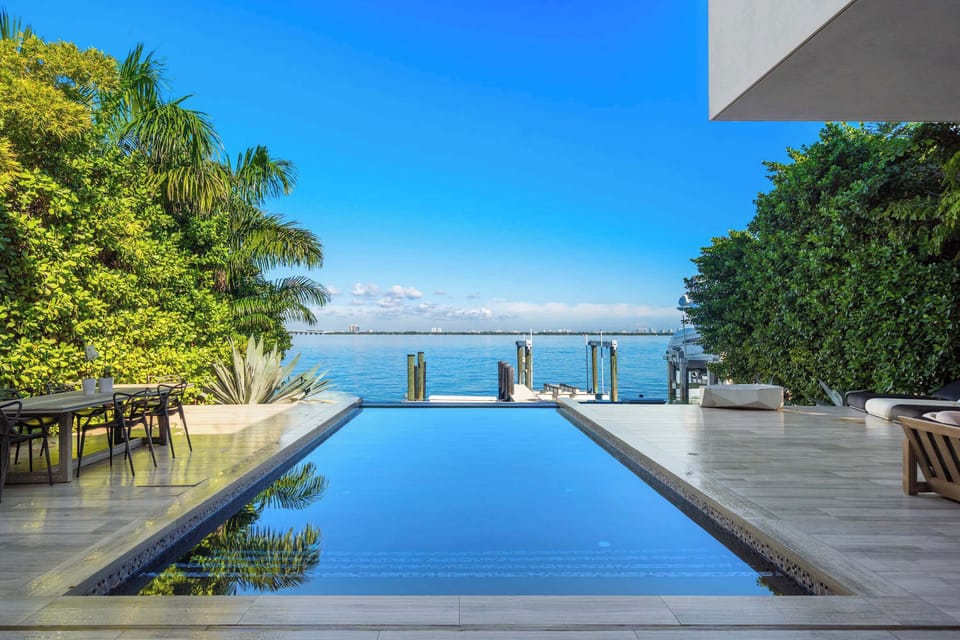 Waterfront pool overlooking the bay with private dock access, expansive sun deck, and tropical landscaping. Contemporary outdoor living space designed for lounging, dining, and enjoying unobstructed water views.