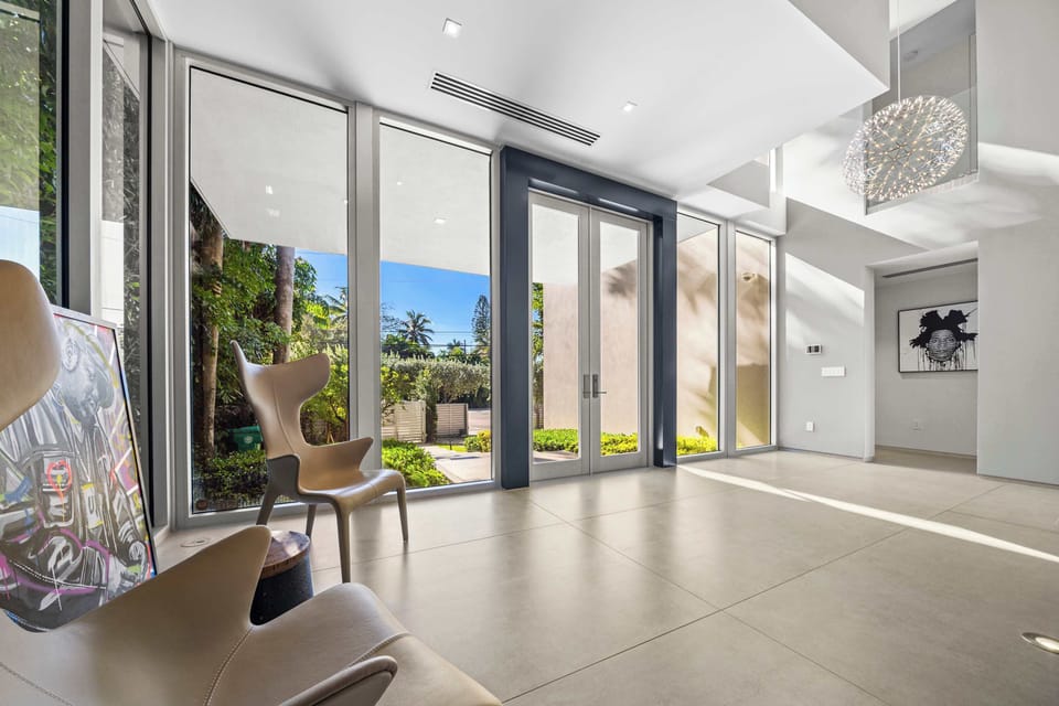 Grand entry foyer featuring floor-to-ceiling glass, double-height ceilings, polished tile flooring, and tropical garden views. Natural light highlights the home's contemporary architecture and open-concept design.