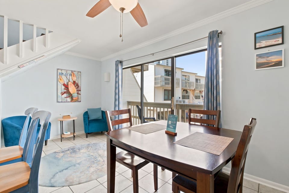 Step into your bright dining area with coastal charm, where meals feel easy and breezy. The table seats your group comfortably, and beyond the sliding doors, your private balcony awaits with ocean-inspired views.