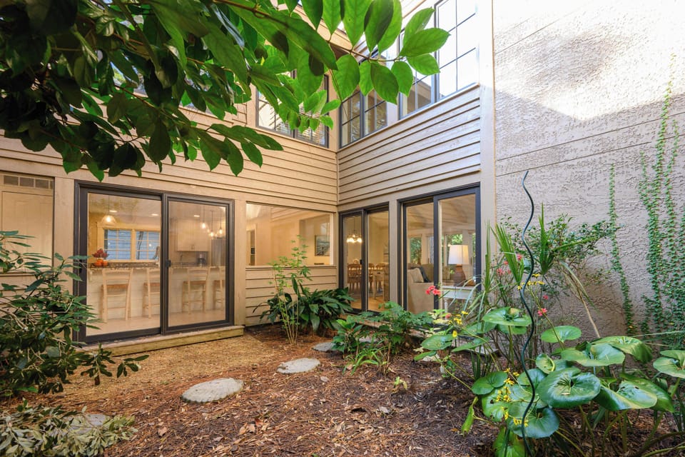 A private, serene courtyard featuring a mix of stone pavers and lush greenery. Large sliding glass doors offer a seamless transition between the indoor living spaces and this tranquil outdoor retreat.