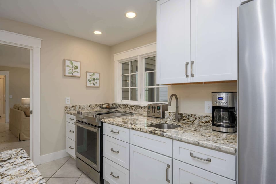 A modern, functional kitchen workspace featuring premium granite countertops, sleek white cabinetry, and high-end stainless steel appliances, including a built-in coffee station.