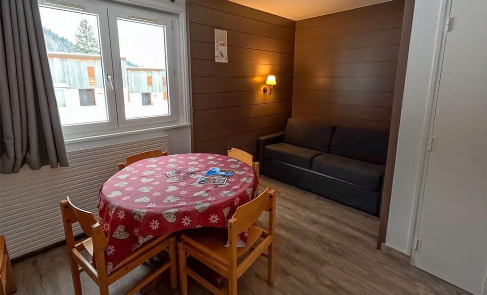 The inviting living space showcases a comfortable sofa and large windows that frame stunning views of the snowy Jura mountains.