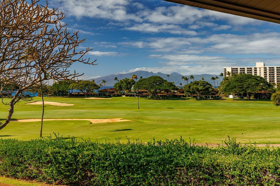 Lush emerald fairways and open mountain‑lined horizons create a picturesque backdrop beneath bright island skies.