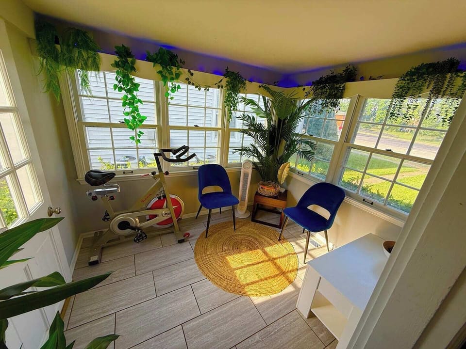 Sunroom office with natural light, a convertible table-to-desk setup, and a workout bike — ideal for work, wellness, or both.